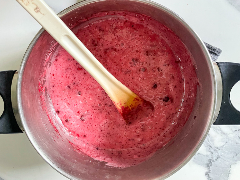 Vibrant pink raspberry and rose marshmallow mixture in a saucepan with a spoon