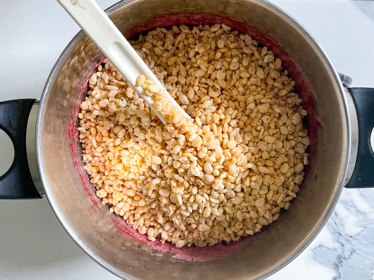 Stirring puffed rice cereal into a pan of melted marshmallow