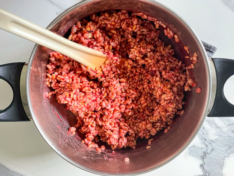 Pink rice krispie treat mixture in a stock pot with a spoon