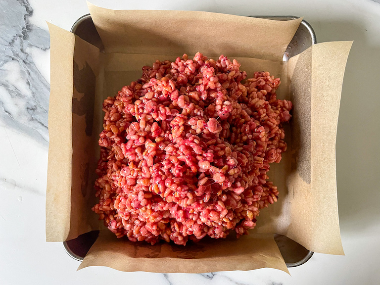 Pink krispie treat mixture in a parchment lined pan