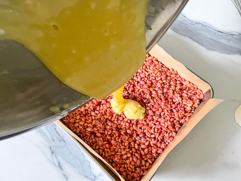 Pouring white chocolate ganache over a pan of pink rice krispie treats
