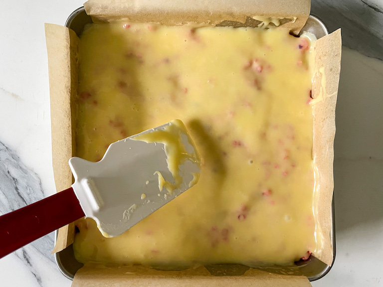 Spatula spreading white chocolate ganache over a pan of rice krispie treats