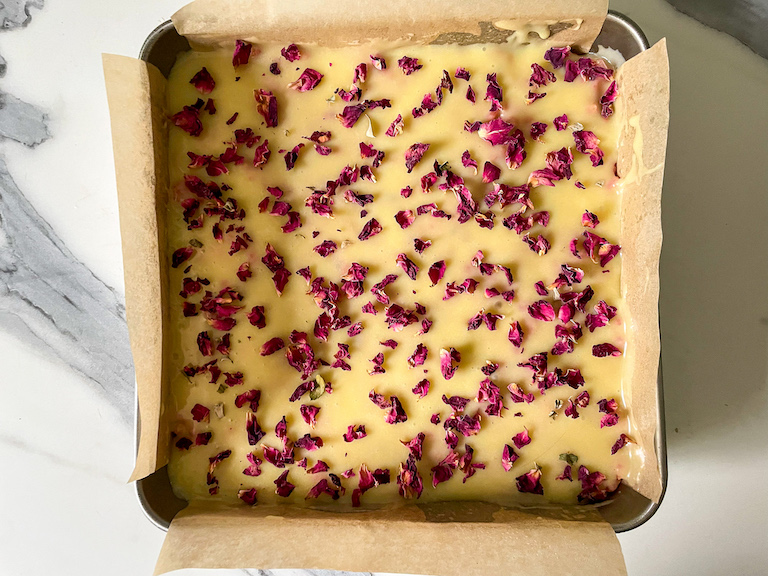 A pan of rice krispie treats decorated with white chocolate ganache and rose petals