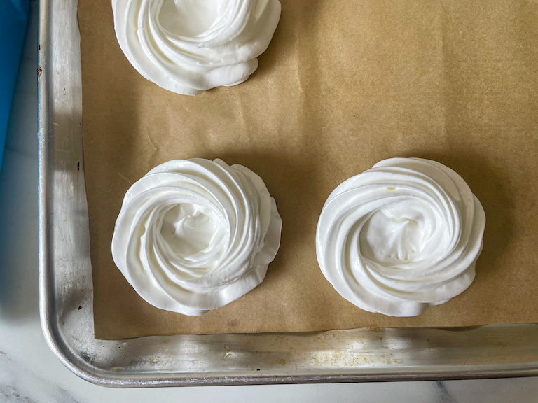 White meringue nests piped on a parchment lined tray