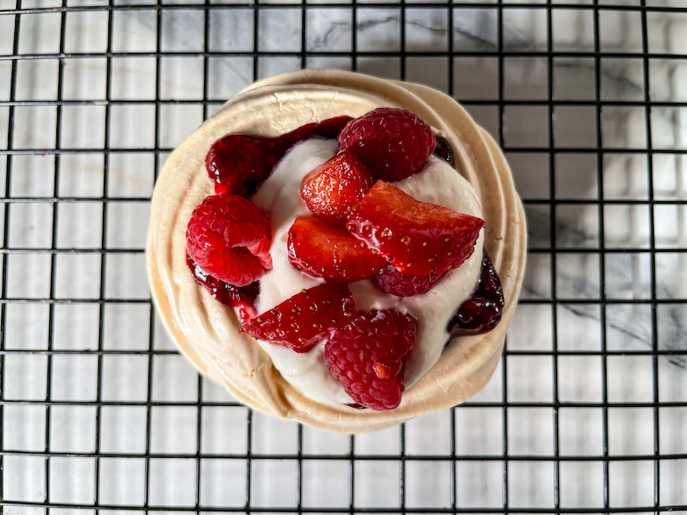 Pavlova decorated with mixed berry compote, whipped cream, and fresh berries 