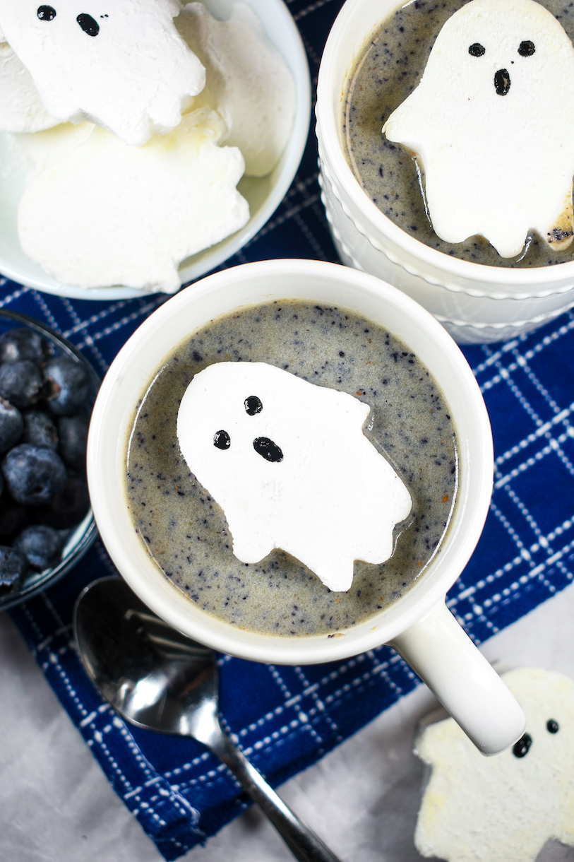 a ghost marshmallow floating on top of a mug of blueberry hot chocolate
