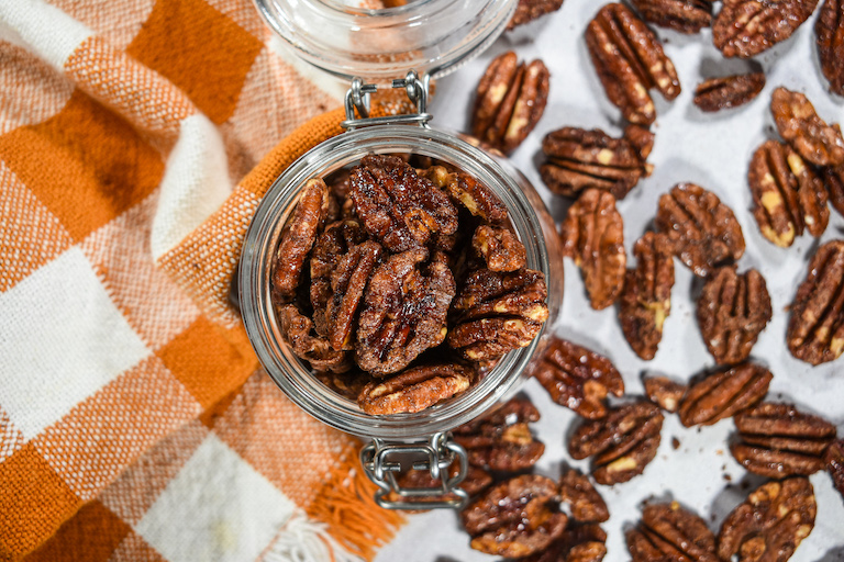 Looking down at a jar of candied pecans with nuts scattered around
