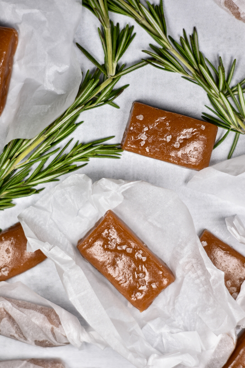 Rosemary caramels on a white surface with sprigs of rosemary
