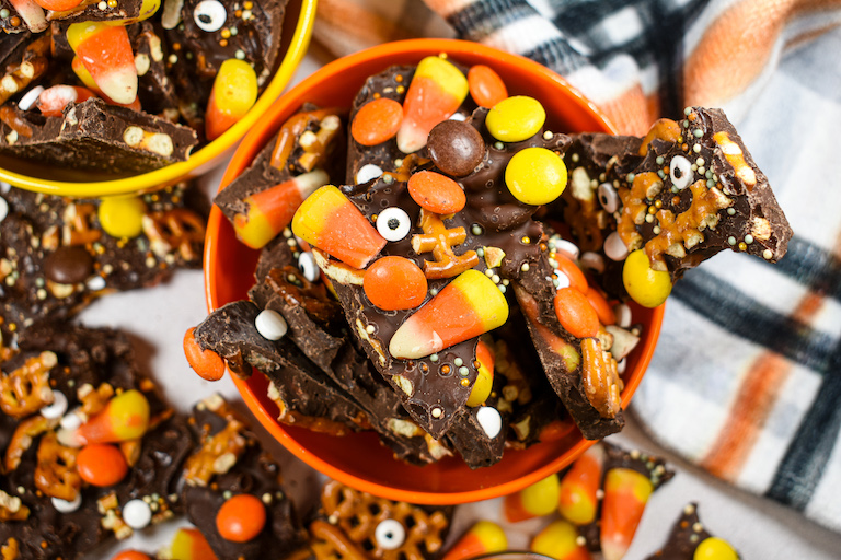 A bowl of Halloween bark on a white surface with a plaid tea towel