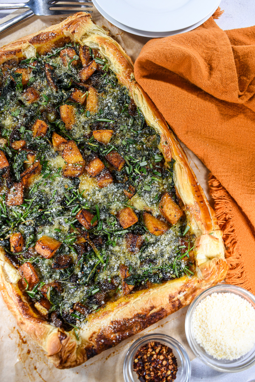 rectangle shaped puff pastry tart with spinach and butternut squash, next to dishes of cheese and chili flakes