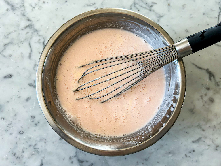 A whisk in a bowl of peppermint ice cream, before churning