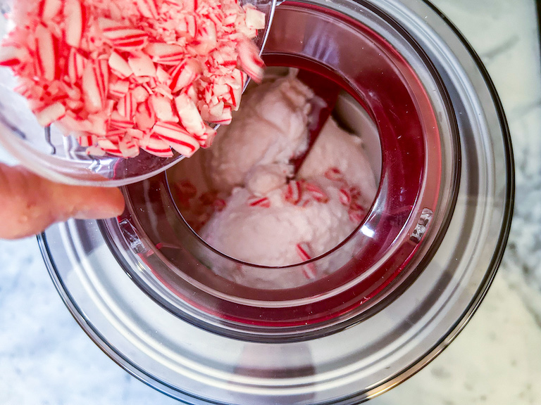 Hand pouring a small dish of candy cane pieces into an ice cream maker