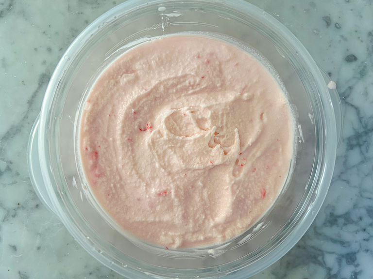 Pale pink peppermint ice cream scooped into a container after churning