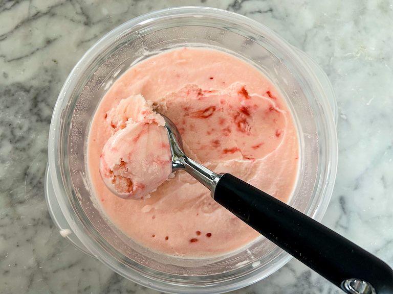 Ice cream scoop in a container of pink peppermint ice cream