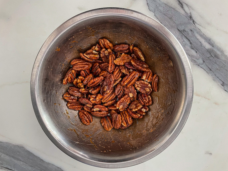 A bowl of maple pecans on a marble surface
