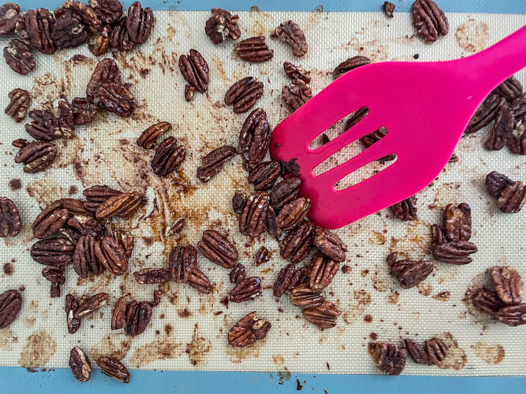 Pink spatula tossing maple glazed pecans on a silicone mat