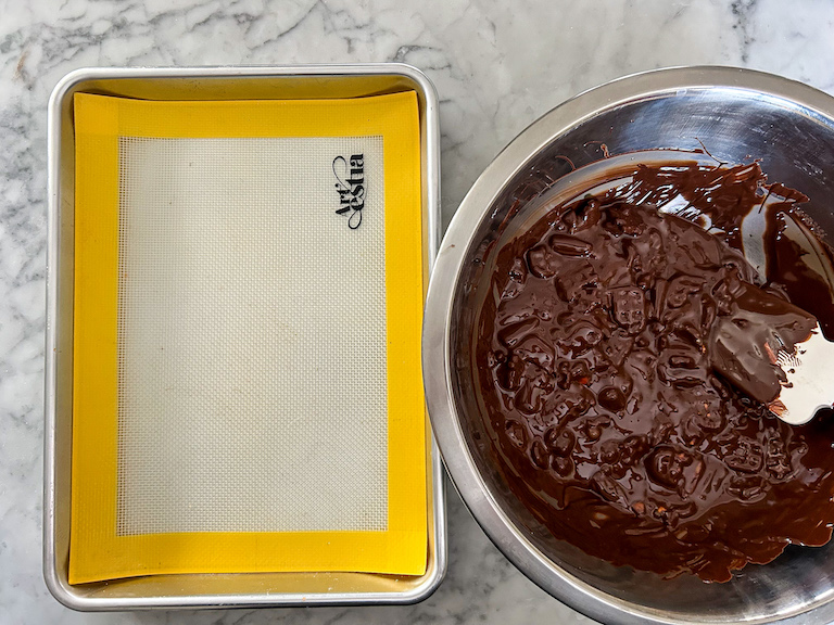 A bowl of melted chocolate and a small tray with a silicone mat