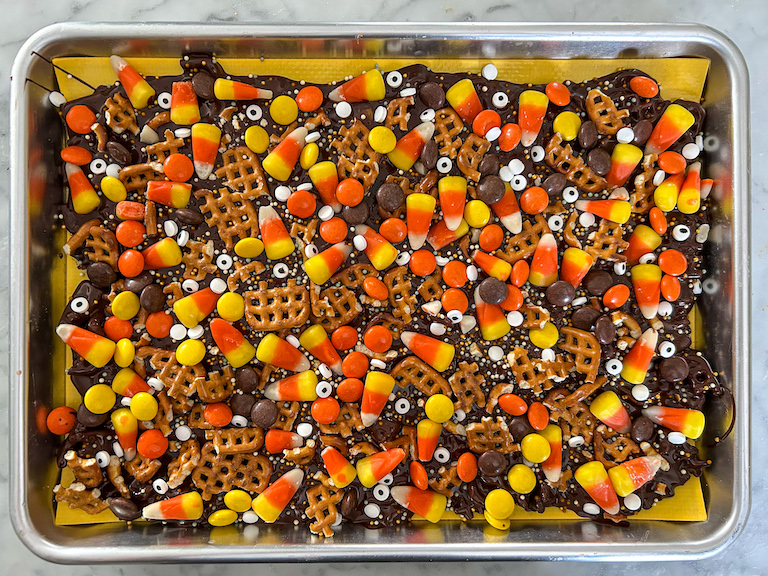 A tray of dark chocolate bark decorated with pretzels, Reese's, candy corn, and candy eyeballs