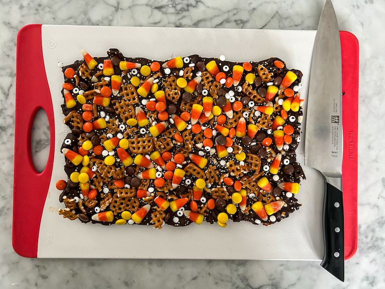 A slab of Halloween candy bark on a cutting board with a knife
