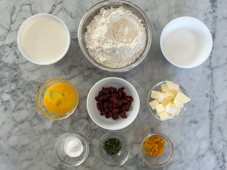 Ingredients for making cranberry and orange scones arranged on a marble surface