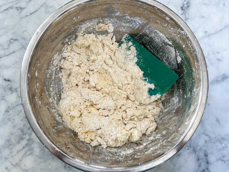 A bowl of scone dough with a green bench scraper