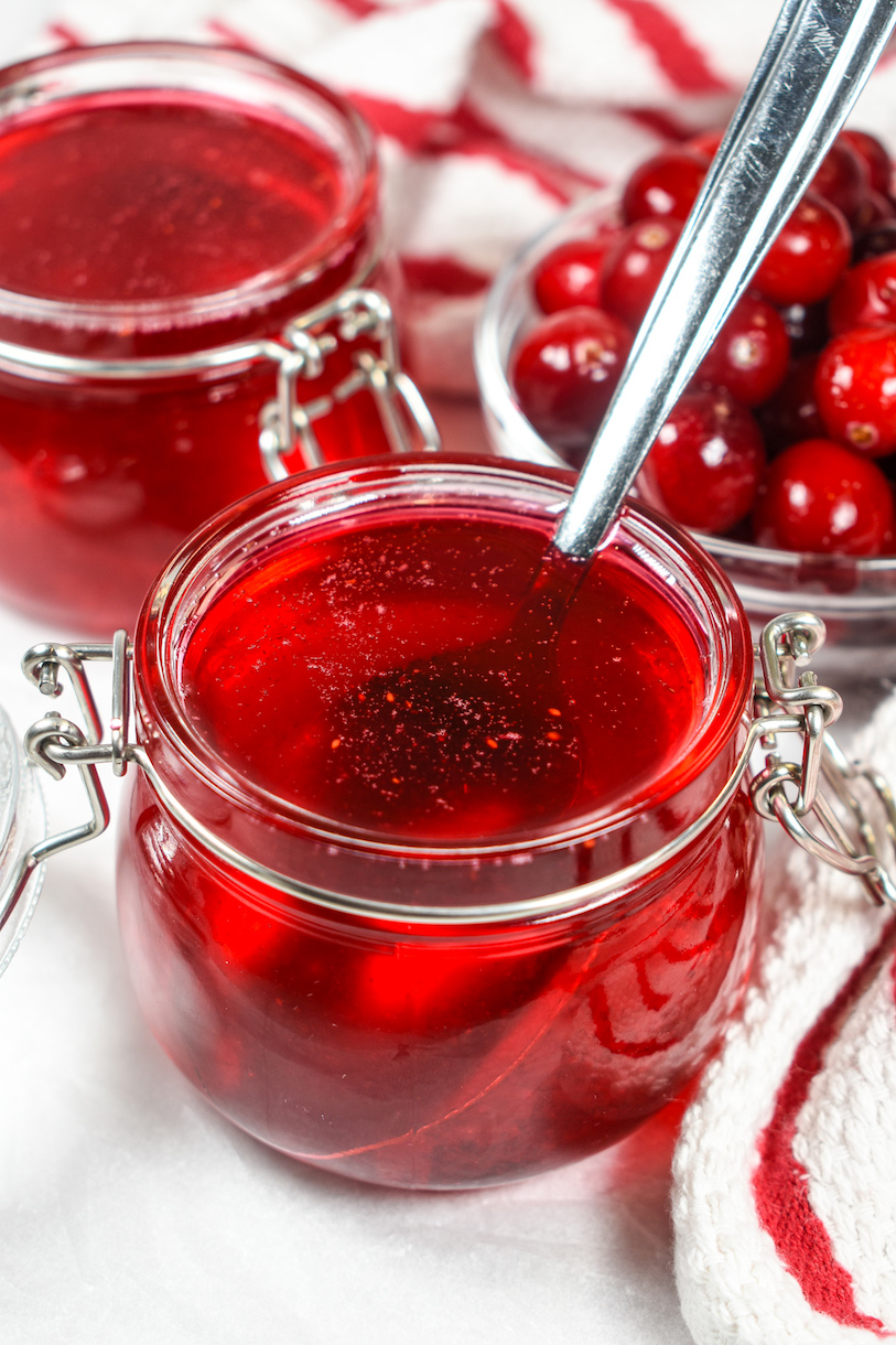 A jar of homemade cranberry syrup with a spoon