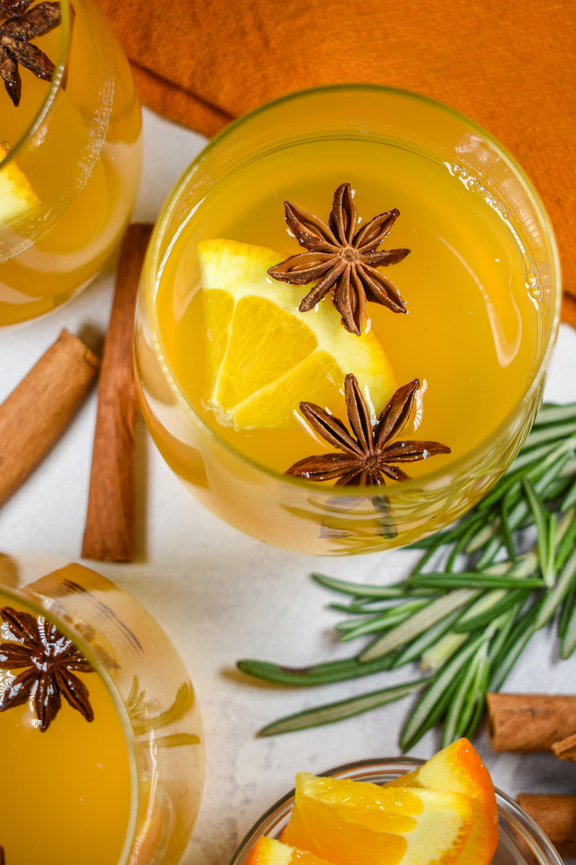 Glasses of mulled white wine surrounded by rosemary sprigs and cinnamon sticks