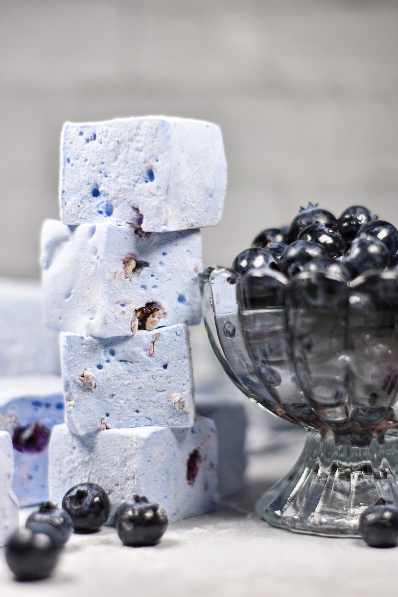 A stack of blueberry marshmallows next to a dish of berries