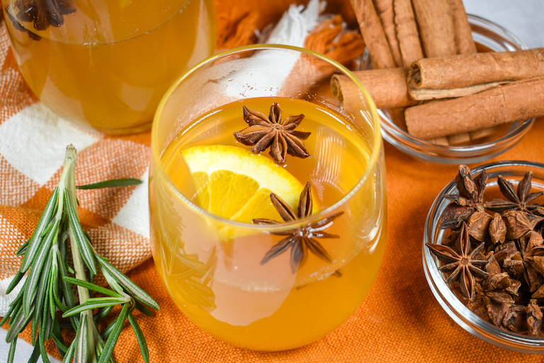 A glass of mulled white wine garnished with star anise and a wedge of orange
