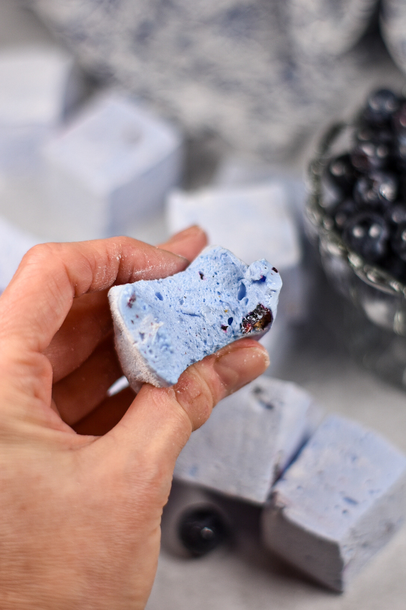 Hand holding a blueberry marshmallow with a bite missing