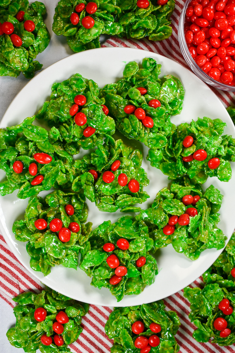A plate of holly leaf cookies arranged on a red and white striped towel