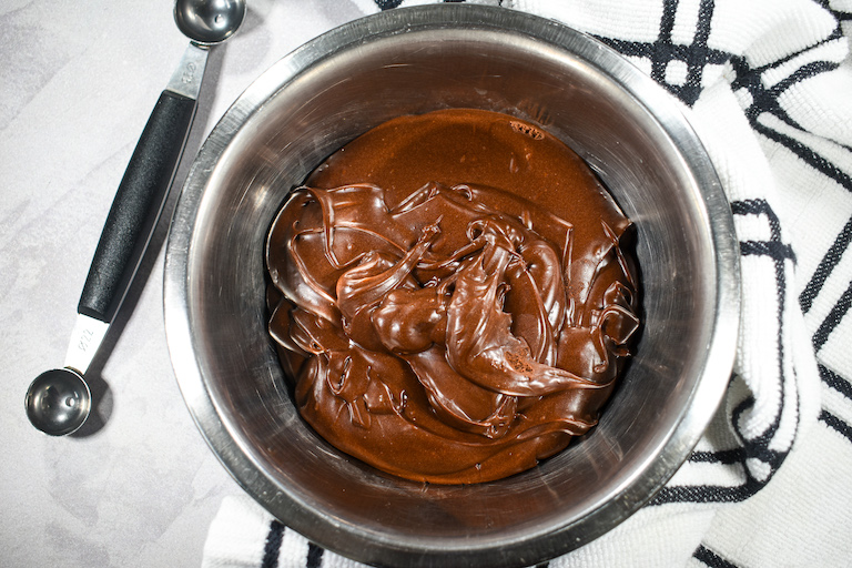 A bowl of dark chocolate ganache, a plaid towel, and a melon baller