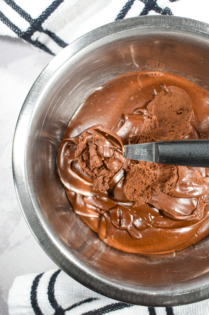 A melon baller in a bowl of dark chocolate ganache