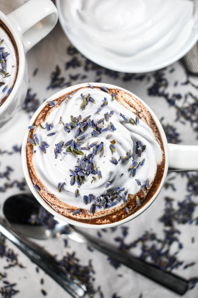 A mug of lavender hot chocolate garnished with whipped cream and bits of dried lavender flowers