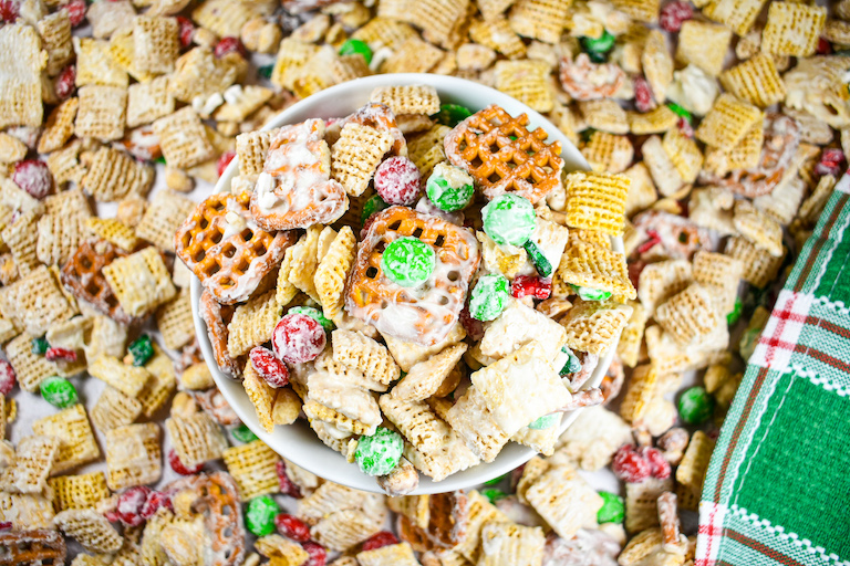 A bowl of Christmas Chex mix surrounded by more cereal mix