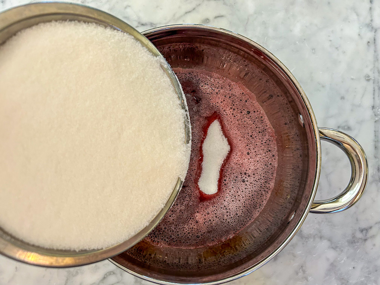Adding granulated sugar to a pan of cranberry juice and gelatin
