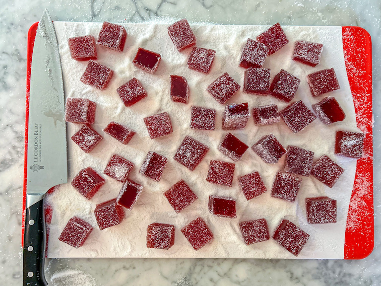 Squares of cranberry candy on a cutting board with a knife