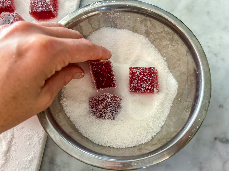 Hand tossing cranberry candy squares in a bowl of sugar