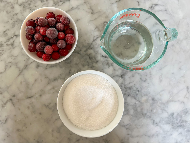 Dishes of cranberries, water, and sugar on a marble surface