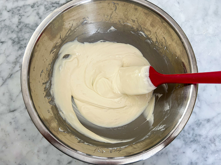bowl of melted white chocolate with a red spatula