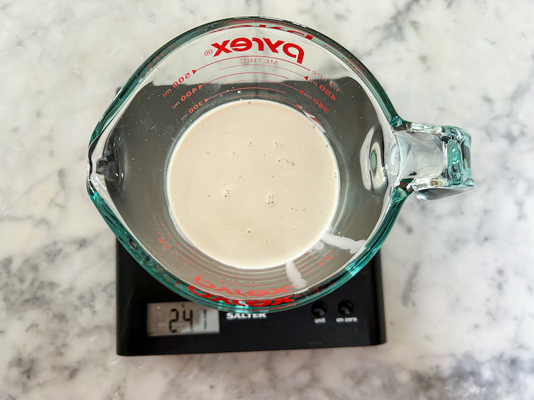 A measuring cup of cream sitting on a kitchen scale