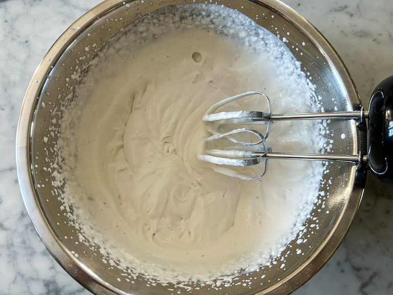 Mixer whipping cream in a large metal bowl