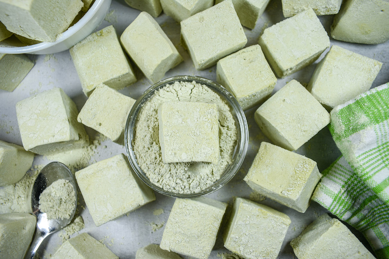 A dish of matcha powder and confectioner's sugar with a matcha marshmallow on top, surrounded by more marshmallows