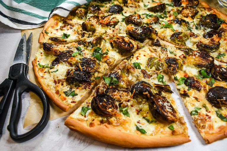 Pizza with roasted brussels sprouts, cheese, and herbs with a pair of kitchen shears