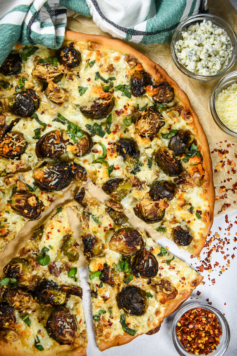 Sliced Brussels sprout pizza alongside dishes of cheese and chili flakes