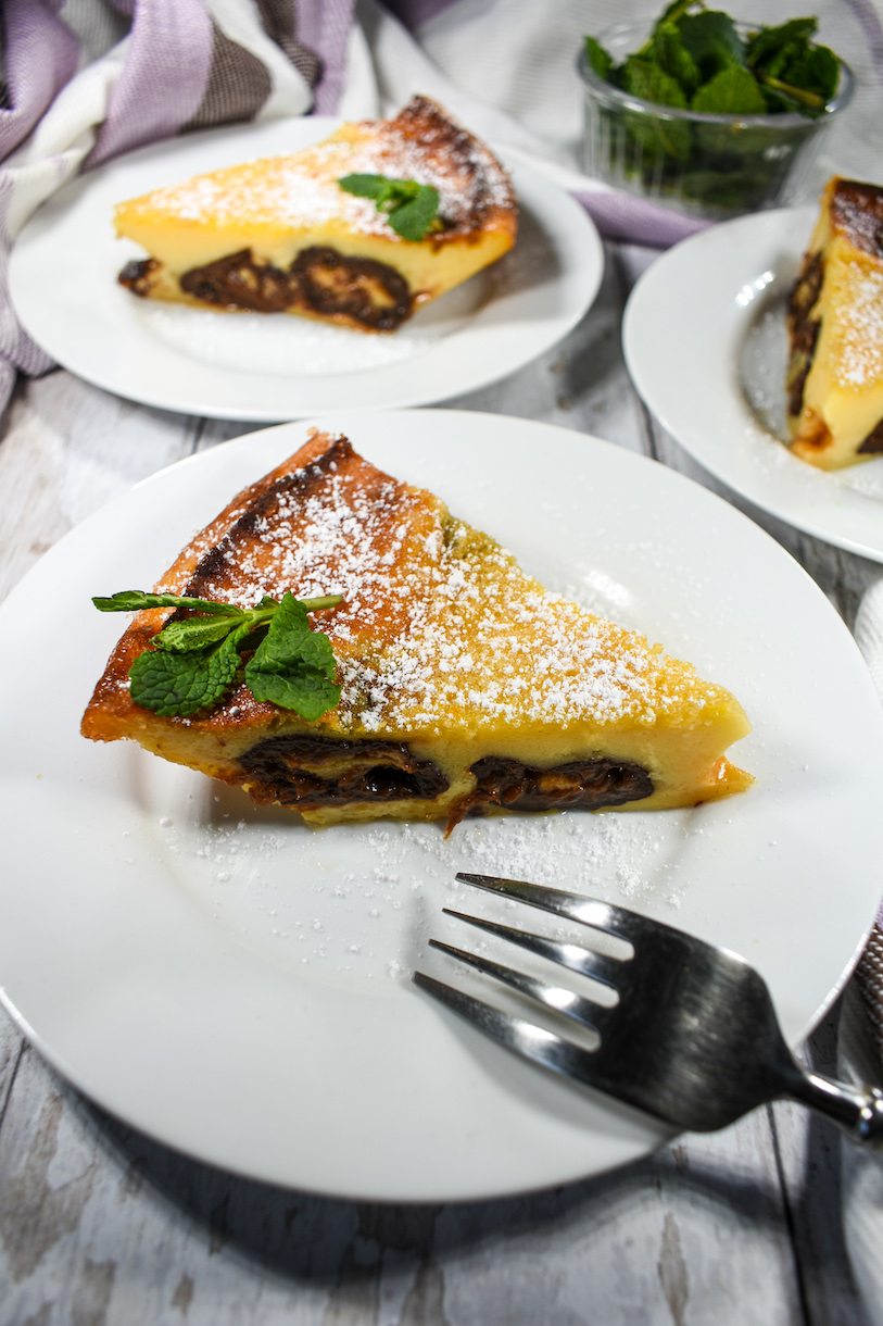Slices of clafoutis on white dessert plates, arranged on a white wooden surface