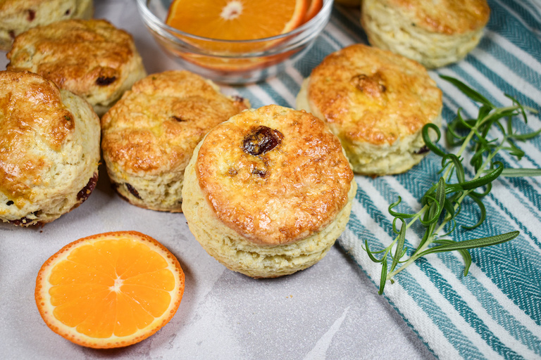 Cranberry scones on a striped tea towel with a sprig of rosemary and an orange slice