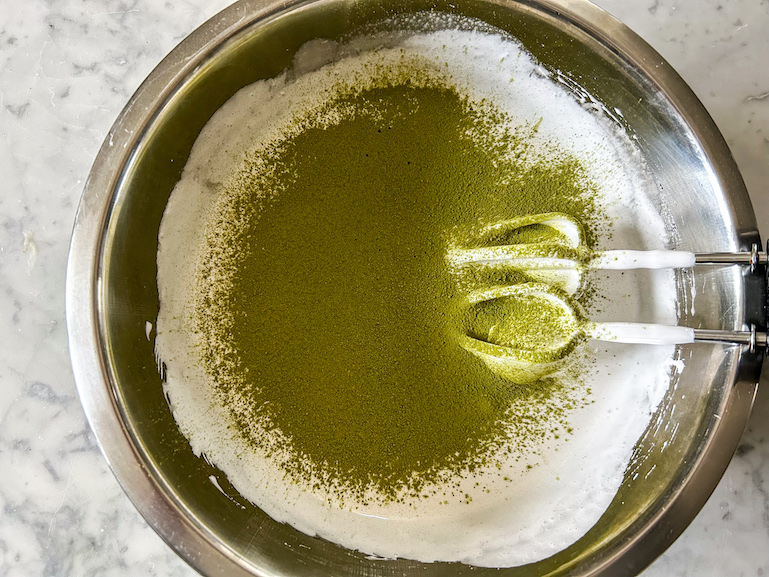 Bright green matcha powder sifted into a bowl of marshmallow fluff