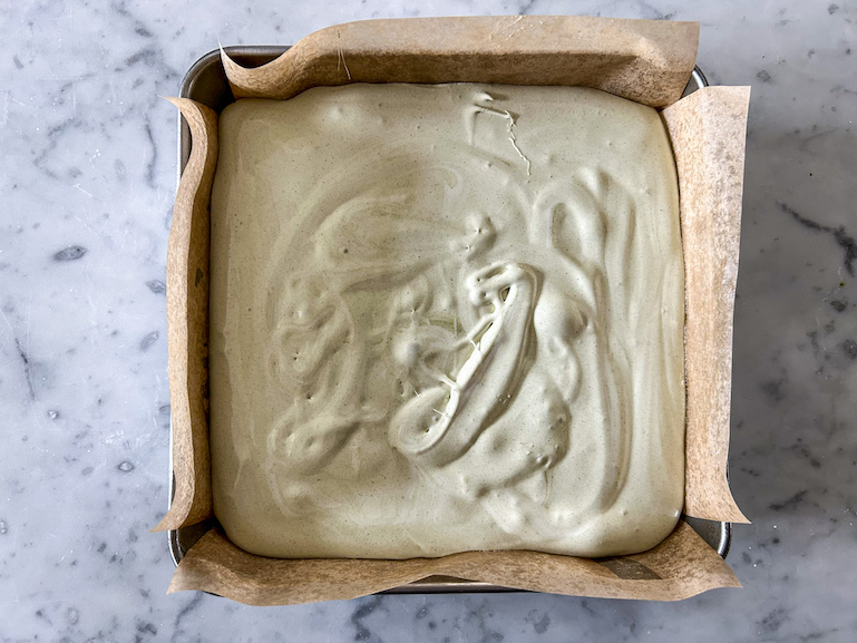A square tin of matcha marshmallows cooling on a marble countertop