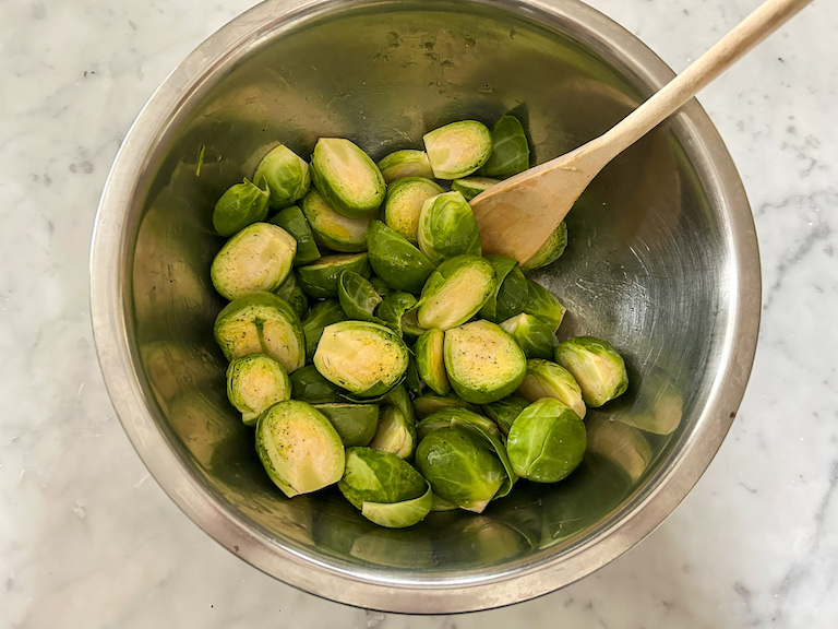A bowl of brussels sprouts tossed in olive oil, with a wooden spoon